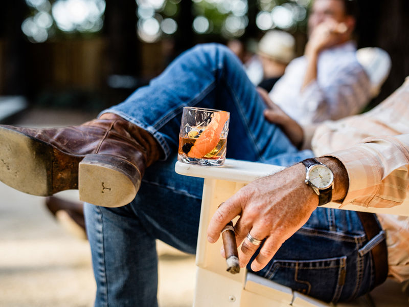 Man relaxing outdoors with a cigar and a drink.